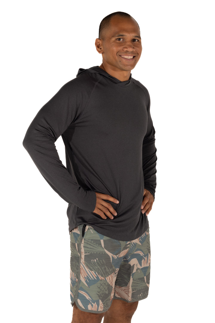 Male model wearing the Waihana Mariner Black Hooded Long Sleeve sun shirt with tropical print board shorts, shown from a slight angle against a white studio background.
