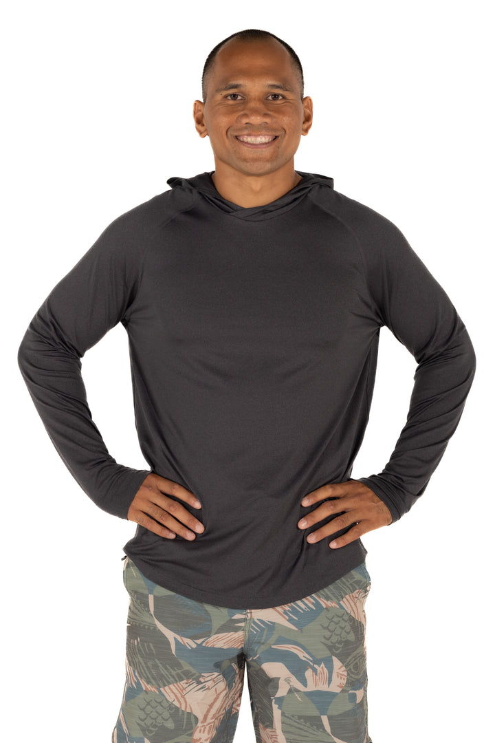 Male model wearing the Waihana Mariner Black Hooded Long Sleeve sun shirt in charcoal, paired with tropical-print board shorts, hands on hips, white studio background.