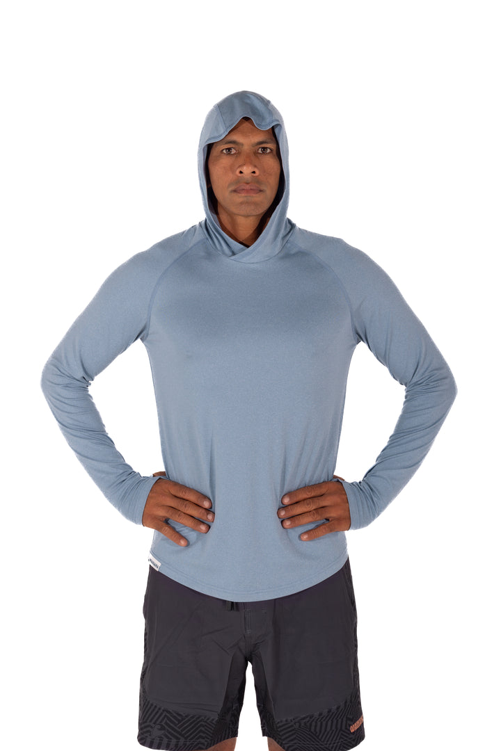 Male model wearing the Waihana Mariner Blue Hooded Long Sleeve sun shirt with dark board shorts, hands on hips, against a white studio background.